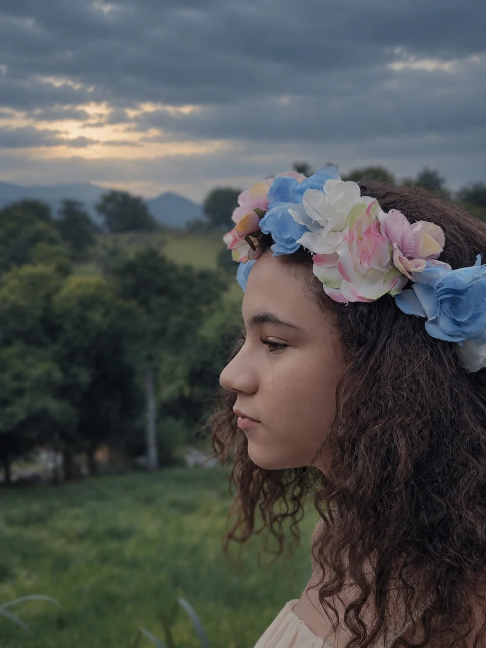 Profile portrait of a woman with flowers in her hair, surrounded by greenery.