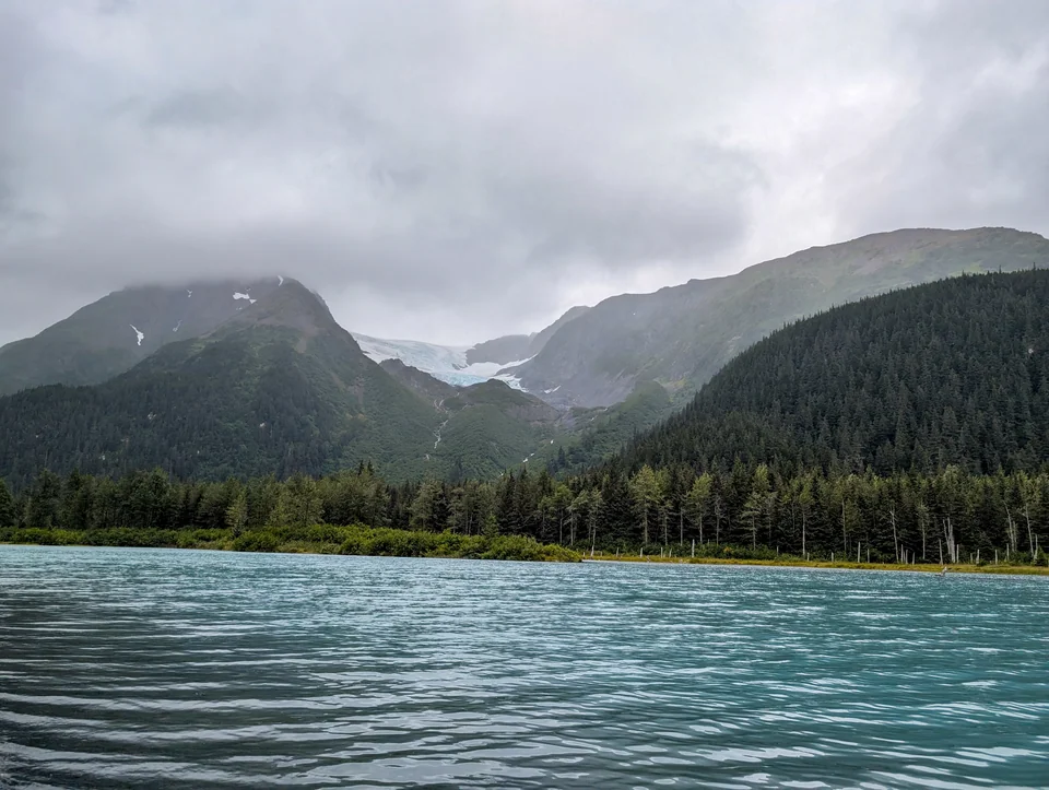 Greenish lake in front of cloud-covered mountains.