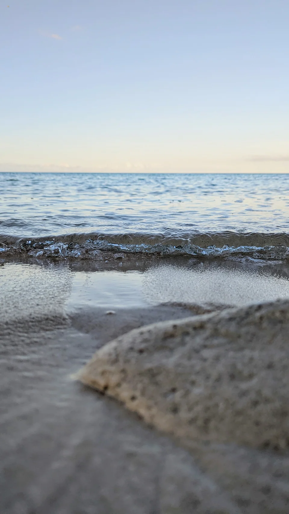 Foam from a wave on the sand, with the sea and the horizon behind.