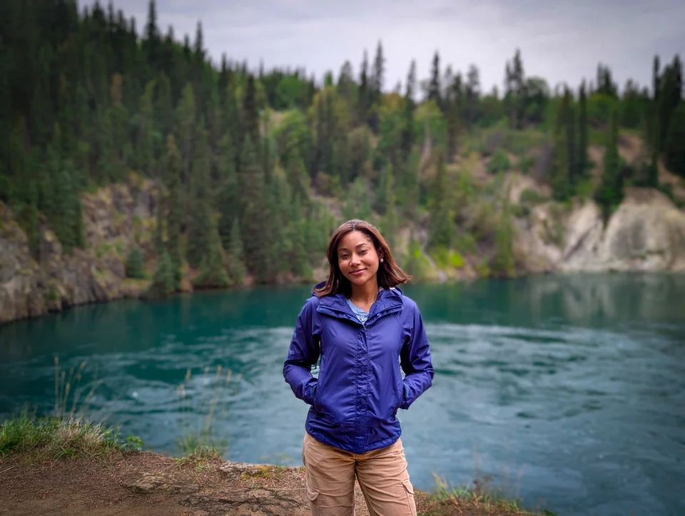 Portrait of a person in a violet jacket in front of a turquoise lake.
