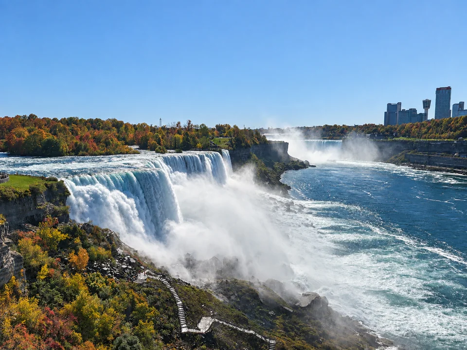 Wide waterfalls among greenery with distant buildings.
