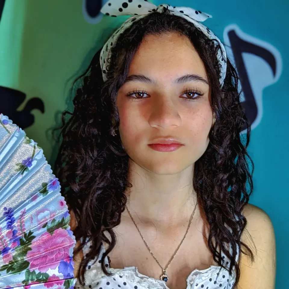 Portrait of a young woman with a scarf in her hair and a fan, on a blue-green background.