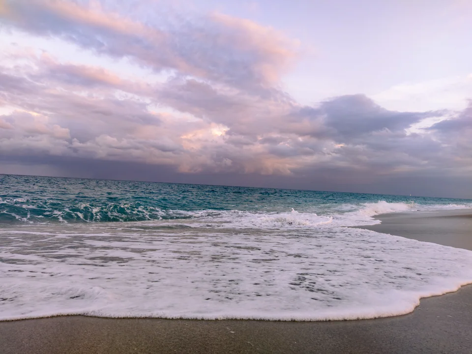 Waves breaking on the beach under a sky of pink and gray clouds.