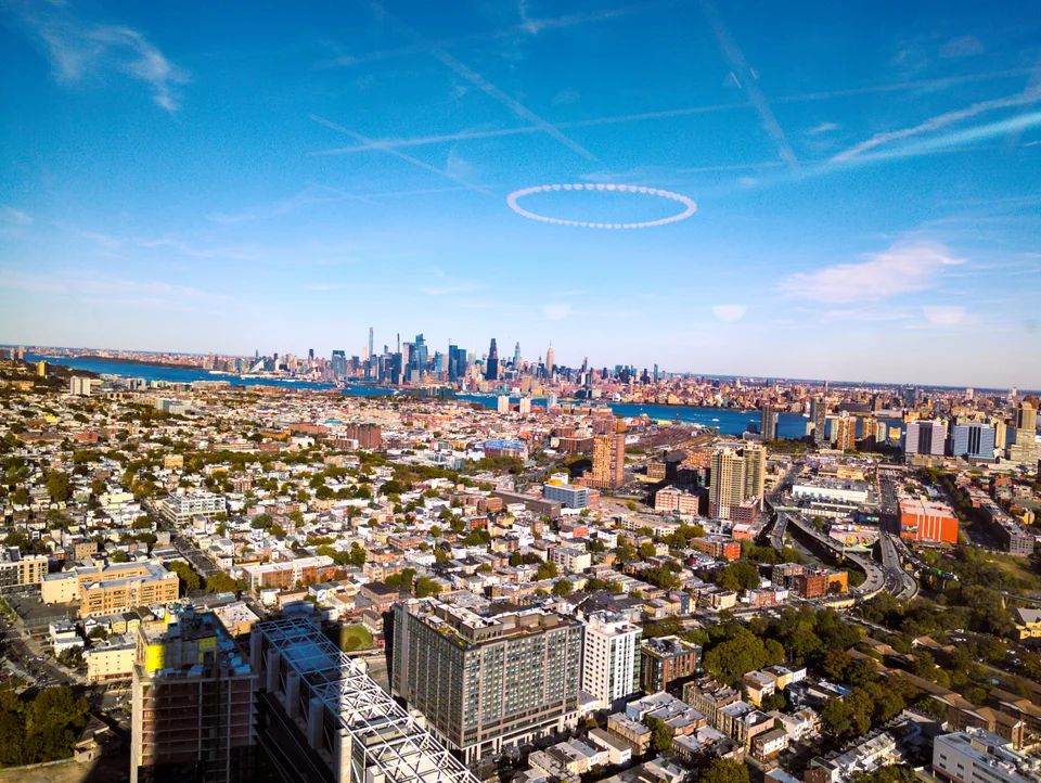 Aerial view of a city with low buildings and skyscrapers in the distance under a blue sky.