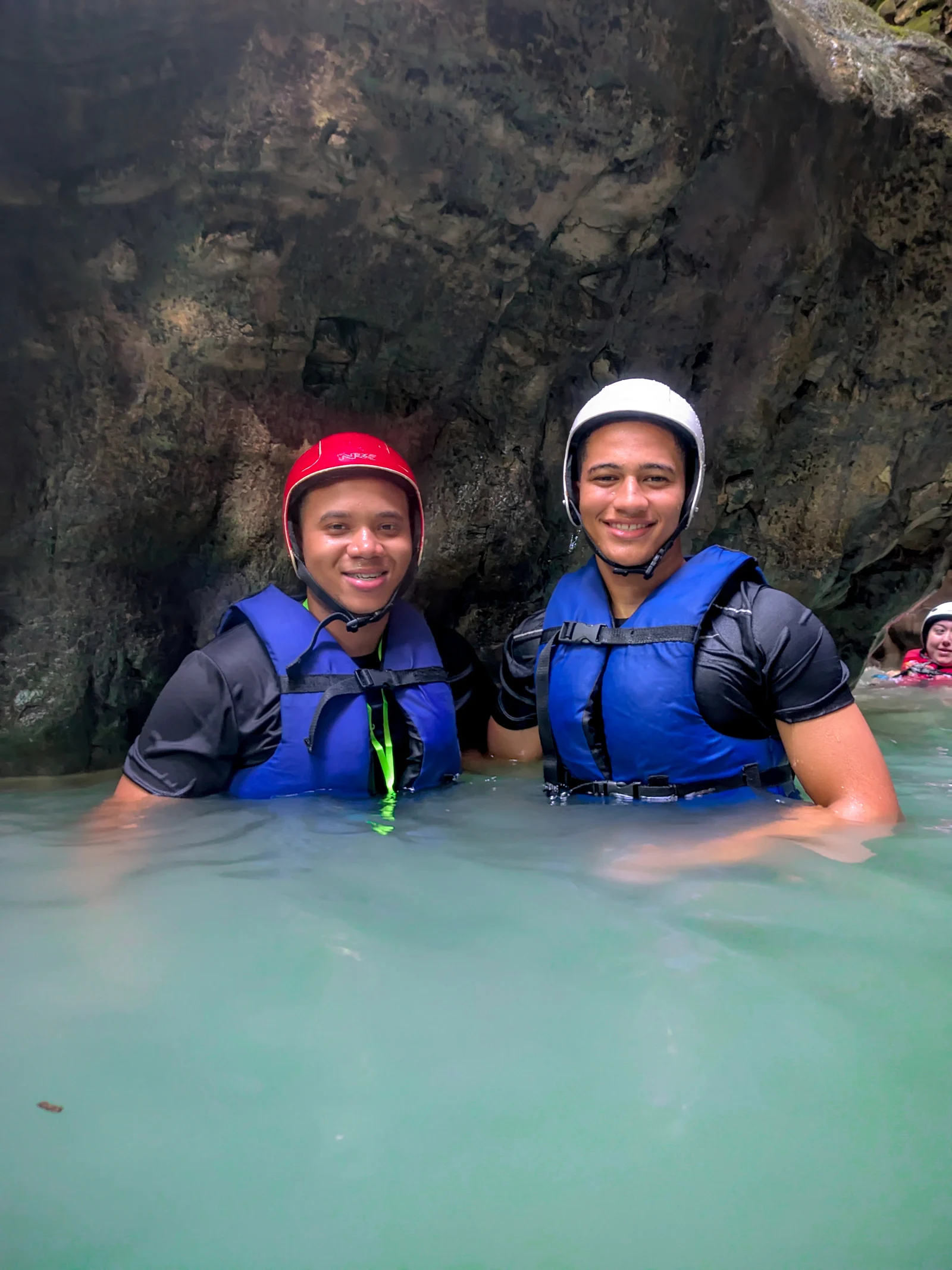Two people in helmets and life jackets in the water, between rock walls